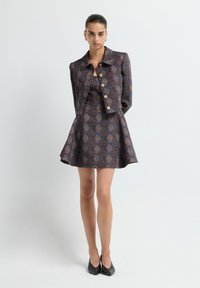 Vestido marrón con estampado, con un corsé ajustado y una falda acampanada, acompañado de una chaqueta corta a juego con grandes botones y un cuello.