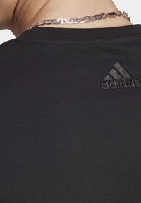 Černé bavlněné tričko s krátkým rukávem, na zadní straně s tonálním výšivkovým logem Adidas a hladkou, jemnou texturou.