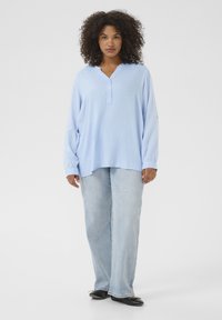 Lichtblauwe overhemd met lange mouwen en een relaxte pasvorm, gecombineerd met lichtblauwe wijde jeans en zwarte ballerina's. Soepele stofstructuur.