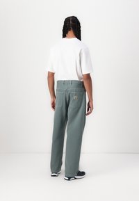Pantaloni gri, largi, cu talie înaltă, două buzunare la spate și un patch cu logo. Asortați cu un tricou alb simplu și adidași închiși la culoare.