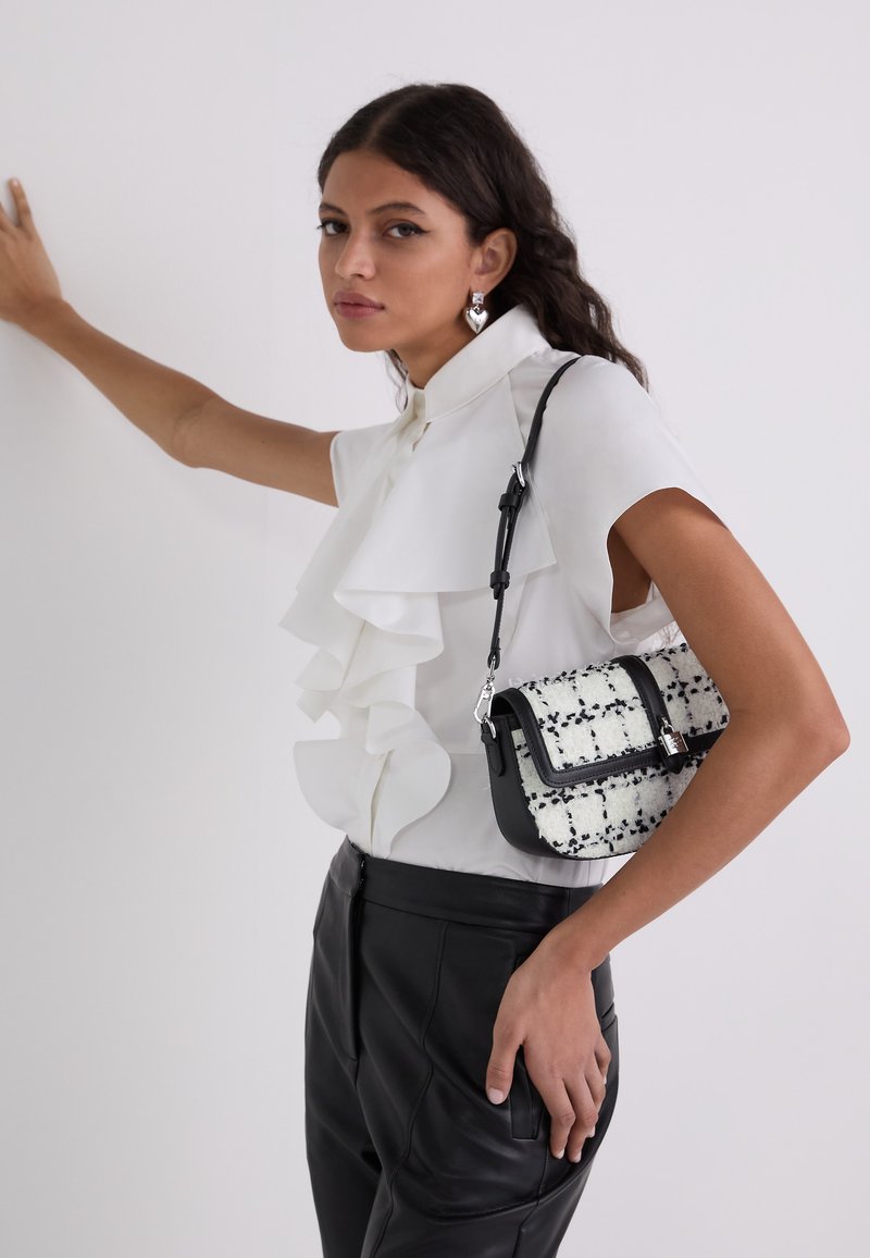 Bluză albă cu volane, cu mâneci scurte, combinată cu pantaloni negri din piele. Accesoriul este o geantă mică din tweed alb-negru cu o curea.