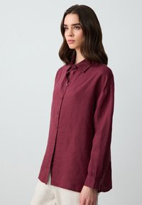 Camicia button-up bordeaux in lino leggero con colletto classico, vestibilità comoda e maniche lunghe, dotata di bottoni ai polsini e superficie testurizzata.