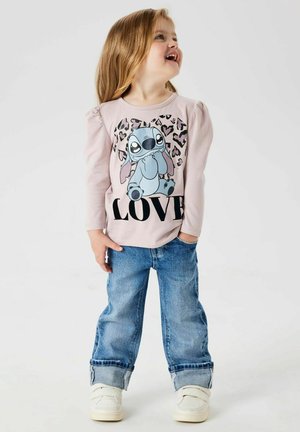 Chemise rose pâle à manches longues avec un personnage de dessin animé et le texte noir "AMOUR", assortie à un jean bleu retroussé et des sneakers blanches.