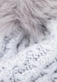Lichtgrijze gebreide sjaal met een gestructureerd patroon en een zachte, pluizige grijze bontafwerking. Focus op de fijne steekdetails en het materiaal.