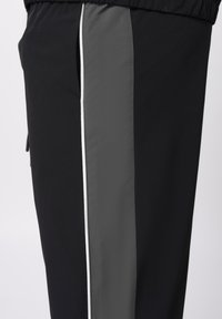 Μαύρο αθλητικό παντελόνι με πλαϊνή λωρίδα σε σκούρο γκρι, δια κοσμημένη με λεπτή λευκή ρίγα. Ομαλή υφή με ελαστική ζώνη μέσης.