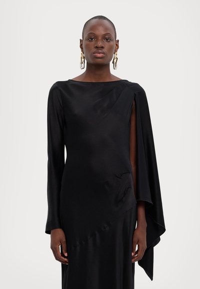 Vestido de satén negro con mangas largas, diseño drapeado asimétrico y detalles con corte en los hombros. Textura suave y fluida. Pendientes de oro.