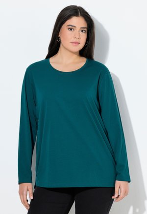 Teal langekleurige T-shirt met lange mouwen, gemaakt van zachte stof, met een ronde hals en een relaxte pasvorm. Zwarte broek maakt de outfit compleet.
