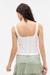 Top bianco senza maniche con spalline larghe, design aderente, tessuto testurizzato e zip centrale sul retro. Abbinato a una gonna verde a strati.