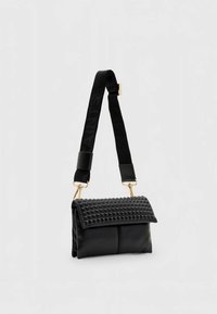 Melnā ādas rokas soma ar gludu virsmu, teksturētu ar kniedēm rotātu pārsegu un auduma siksnu ar reljefiem burtiem. Dzeltens metāla aksesuāri.