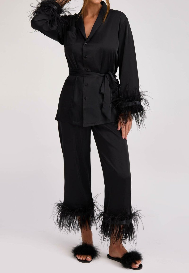 Czarny satynowy komplet piżamowy składający się z koszuli zapinanej na guziki z puchatymi mankietami, dopasowanych spodni z puchatymi wykończeniami oraz futrzanych klapek.