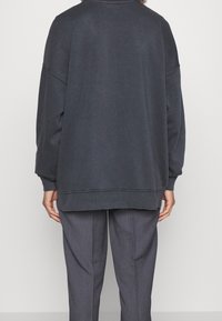 Felpa grigia scura in formato oversized, caratterizzata da maniche lunghe, polsini a costine e un collo rotondo, abbinata a pantaloni grigi su misura.