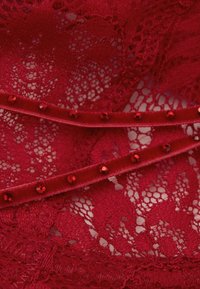 Czerwona koronkowa tkanina z kwiatowym wzorem, warstwowa z czerwoną aksamitną wstążką z małymi czerwonymi cyrkoniami wzdłuż krawędzi.