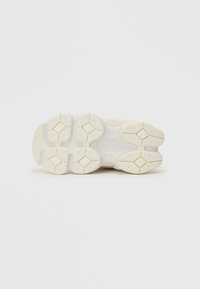 Biela podrážka tenisky má textúrovaný gumový materiál s trojuholníkovými a diamantovými vzormi, ktoré zabezpečujú trakciu a stabilitu.