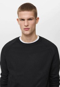 Črn teksturiran pulover s krožnim ovratnikom in raglan rokavi. Ima bel notranji ovratnik in gladko površino.