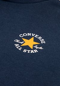 Ύφασμα σκούρου μπλε με λευκό και κίτρινο λογότυπο Converse All Star με αστέρι, περιβαλλόμενο από το κείμενο "CONVERSE Chuck Taylor ALL STAR."