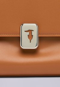 Hnědá kožená kabelka s obdélníkovým stříbrným zapínáním s výřezem, hladkou texturou a elegantním, strukturovaným tvarem.