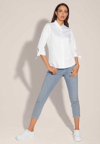Witte blouse met driekwart mouwen en knoopjes aan de manchetten, gecombineerd met lichtblauwe cropped jeans en witte sneakers. Gladde stoftextuur.