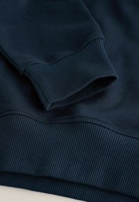 Poignet et ourlet de sweat-shirt bleu marine foncé avec texture en maille côtelée, montrant des détails en gros plan du tissu et des coutures.