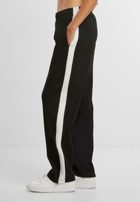 Mustad mustad püksid valgete külgtriipudega, valmistatud pehmest kangast, elastse talje ja küljetaskutega, kantud valgete tossudega.