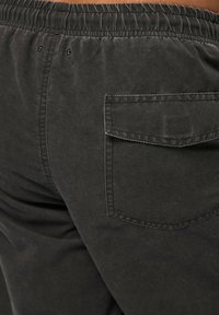 Donkergrijze broek met een zachte textuur, voorzien van een elastische tailleband en een enkele achterzak met klepsluiting.