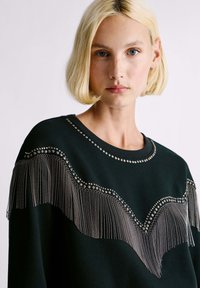 Felpa nera con frange argentate e dettagli con borchie lungo il colletto, con una texture liscia e un design a vestibilità ampia.