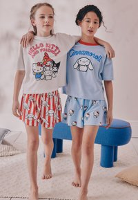 Deux enfants portent des vêtements d'intérieur assortis : un t-shirt blanc avec un motif "Hello Kitty" et un t-shirt bleu avec "Cinnamoroll", assortis à des shorts à motifs.