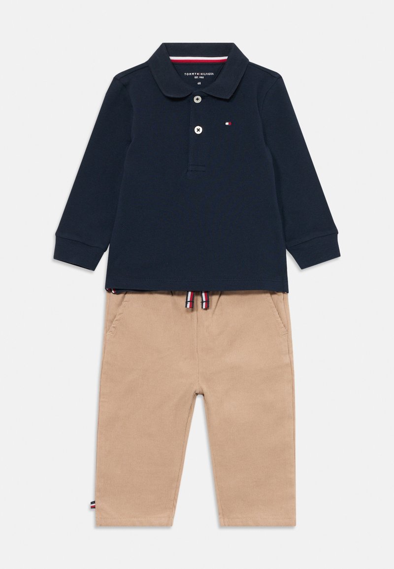 Polo de manga longa azul-marinho com um fecho de botão duplo e um pequeno logótipo, combinado com calças beige com cordão, que apresentam bolsos laterais e detalhes contrastantes.