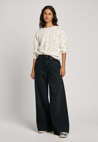 Romantische gebreide crème sweater met een textuurdesign, gecombineerd met wijde, donkere spijkerbroek met zilveren hardwaredetails en subtiele borduursels.
