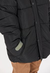 Giacca a vento nera con design trapuntato, colletto rotondo e bottoni a pressione. Presenta un accento in gomma vicino alla tasca, il tessuto ha una texture liscia.