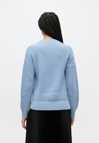 Hele sinine kootud kampsun tekstuurse mustriga, millel on lõdva istuvusega, pikad varrukad ja soonikkoes ääris, kombineeritud volditud musta seelikuga.