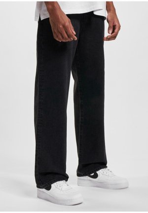 Pantalones de mezclilla negros con un corte recto, diseño de cinco bolsillos y detalles de costura, combinados con zapatillas blancas con acentos en negro.