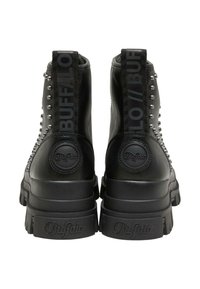 Paire de bottines en cuir noir avec semelles épaisses, clous en métal sur les côtés, et languettes de tirage et logos sur le talon portant la marque "Buffalo."