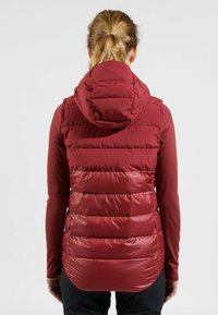 Rote isolierte Weste mit Kapuze, ausgestattet mit einem gesteppten Design und glatter Textur. Der Rücken hat einen längeren Schnitt für zusätzlichen Schutz.