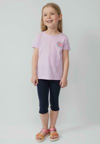 Lichtpaarse katoenen t-shirt met een watermeloenafbeelding en tekst; gecombineerd met marineblauwe legging met een gegolfde zoom; sandalen met roze en oranje banden.