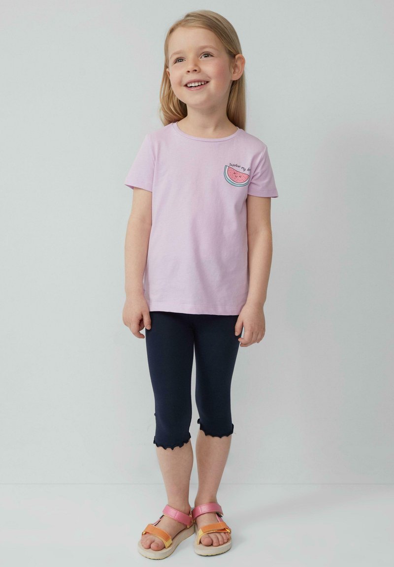Lichtpaarse katoenen t-shirt met een watermeloenafbeelding en tekst; gecombineerd met marineblauwe legging met een gegolfde zoom; sandalen met roze en oranje banden.