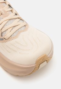 Scarpa atletica beige con tomaia in maglia e motivi texture, lacci piatti e suola in gomma con un leggero tacco.