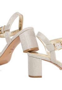 Sandalen met blokhak en banden in lichtgoud textiel. Heeft een metalen gesp en een gladde voering. Vierkante hakontwerp.