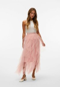 Gonna in tulle rosa con volant a strati e vita elastica, abbinata a una maglietta bianca aderente. Indossata con scarpe a blocco con tacco di colore chiaro.
