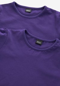 Des t-shirts en coton violet, l'un avec des manches bouffantes, présentent des encolures rondes et une finition cousue. Les étiquettes présentes proviennent de NEXT, indiquant la marque.