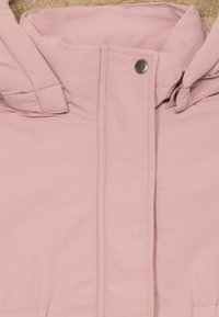 Giacca isolante rosa chiaro con cappuccio, foderata in modo morbido e chiusure a pressione. Texture liscia con dettagli di cucitura visibili.