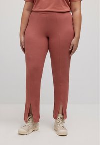 Roodbruin geribde broek met een getailleerd ontwerp, met splits bij de enkels, gedragen met lichtbeige veterschoenen.