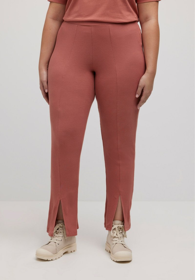 Roodbruin geribde broek met een getailleerd ontwerp, met splits bij de enkels, gedragen met lichtbeige veterschoenen.