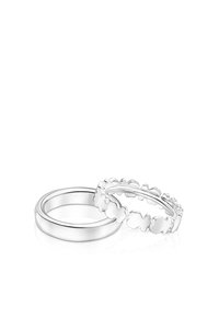 Dos anillos de plata: uno es una banda lisa y el otro tiene bordes festoneados con formas florales. Ambos tienen un acabado pulido.