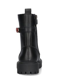 Stivaletto in pelle nera con punta rotonda, suola testurizzata, zip laterale e gemma rossa decorativa sulla tracolla. Suola in gomma piatta.