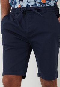 Shorts bleu marine en tissu texturé, avec une taille élastique et un cordon de serrage ajustable. Bords ourlés, poches latérales et coupe droite.
