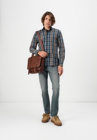 Geruite shirt in blauw, bruin en crème; bruine leren schoudertas; lichtblauwe spijkerbroek; tan schoenen met rubberen zolen en strikjes.