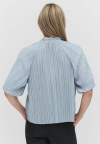 Jasnoniebieska koszula w paski z wysokim kołnierzem, krótkimi bufkami, plisowanym materiałem i małym guzikiem z tyłu.