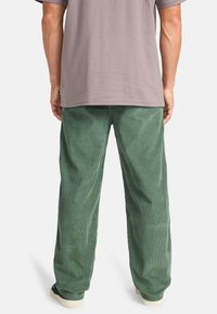 Green corduroy pants with a wide-leg design and vertical ribbed texture, paired with a gray short-sleeve shirt.