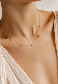 Collier en chaîne dorée mettant en valeur cinq petits accents en forme de papillon avec des détails en pierre claire, porté au niveau de la clavicule sur la peau.