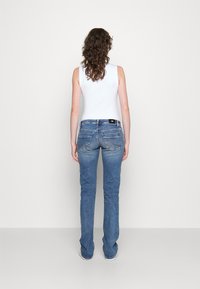 Haut blanc sans manches ajusté et jean en denim bleu clair. Le jean présente une coupe légèrement évasée au bas et des poches arrière avec une couture discrète.